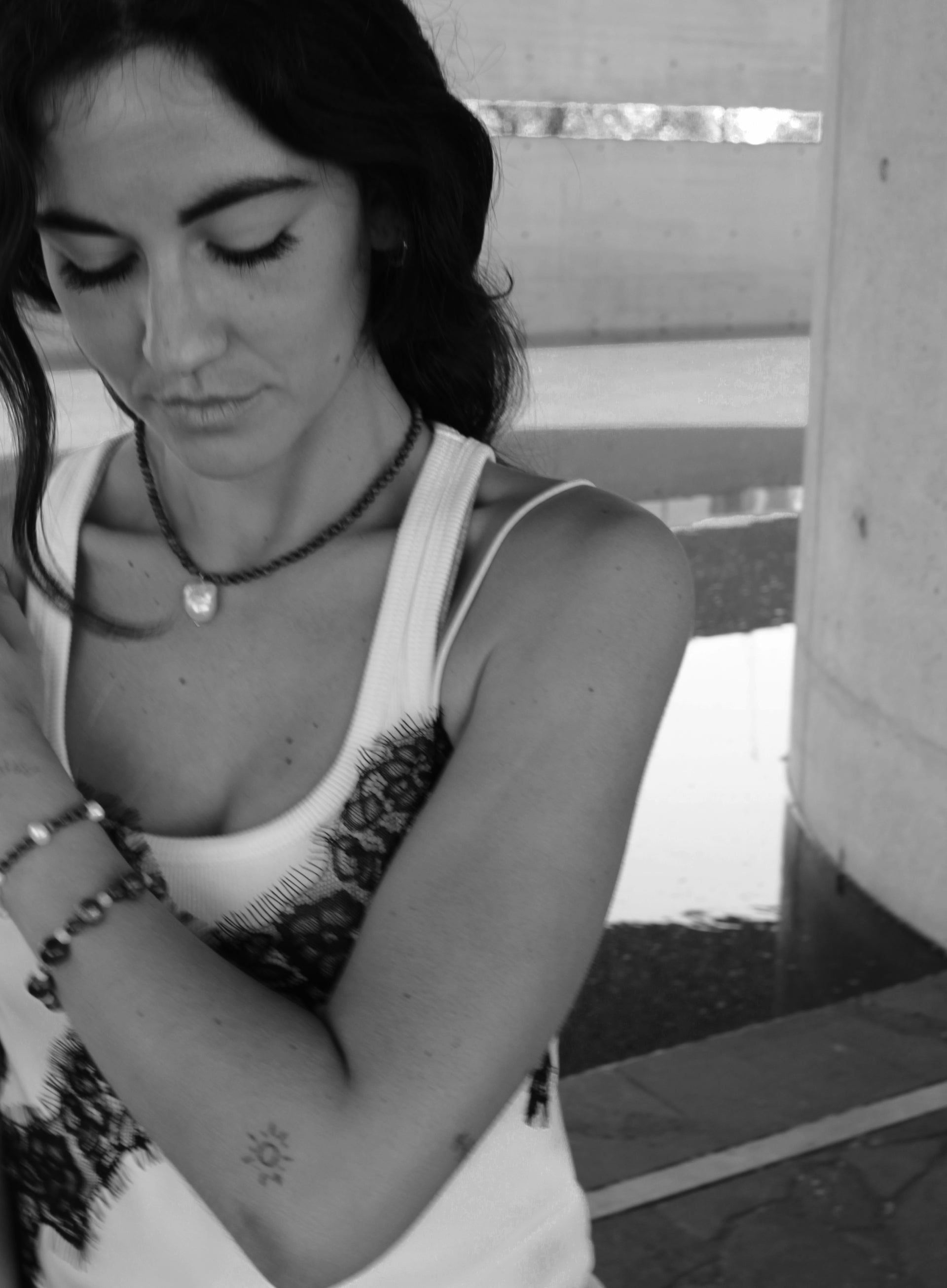 Woman with a ponytail wearing a blue beaded necklace and baraoque pearl charm and white top.