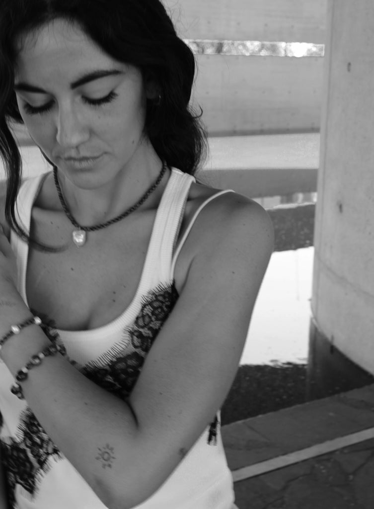 Woman with a ponytail wearing a blue beaded necklace and baraoque pearl charm and white top.