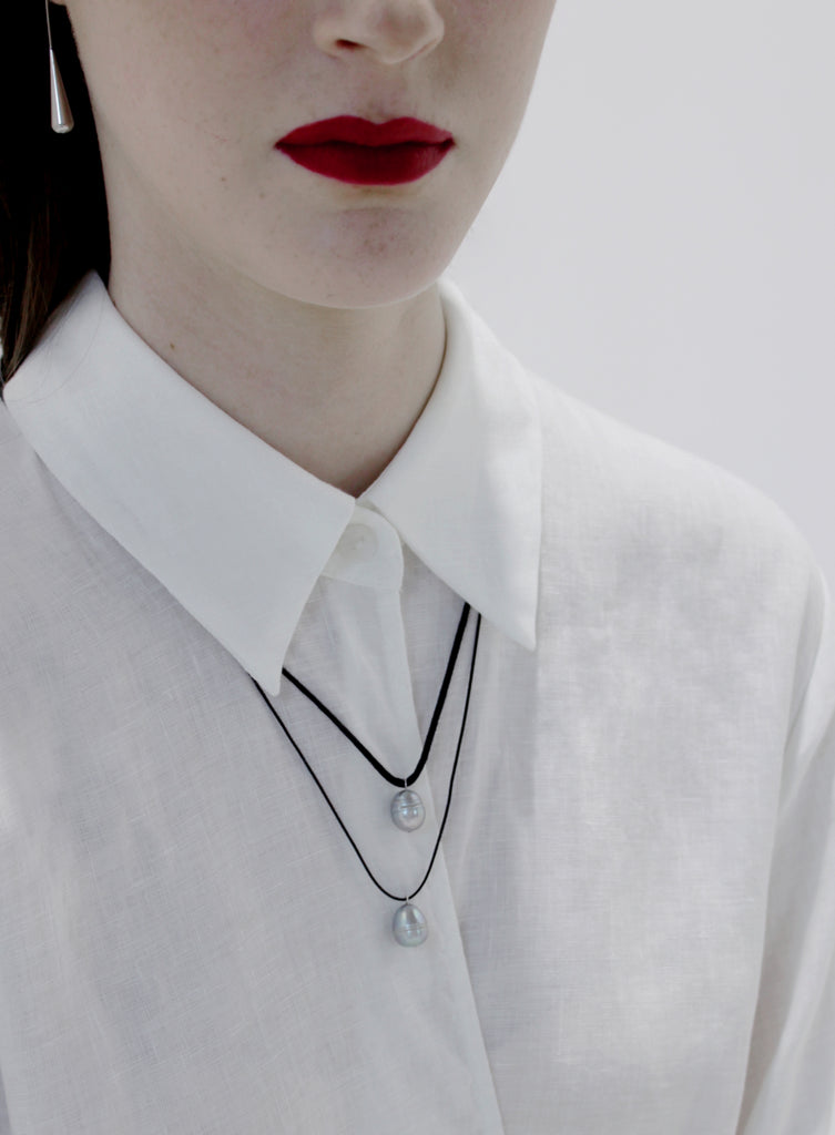 Person wearing a white shirt with a black necklace featuring a pearl pendant.