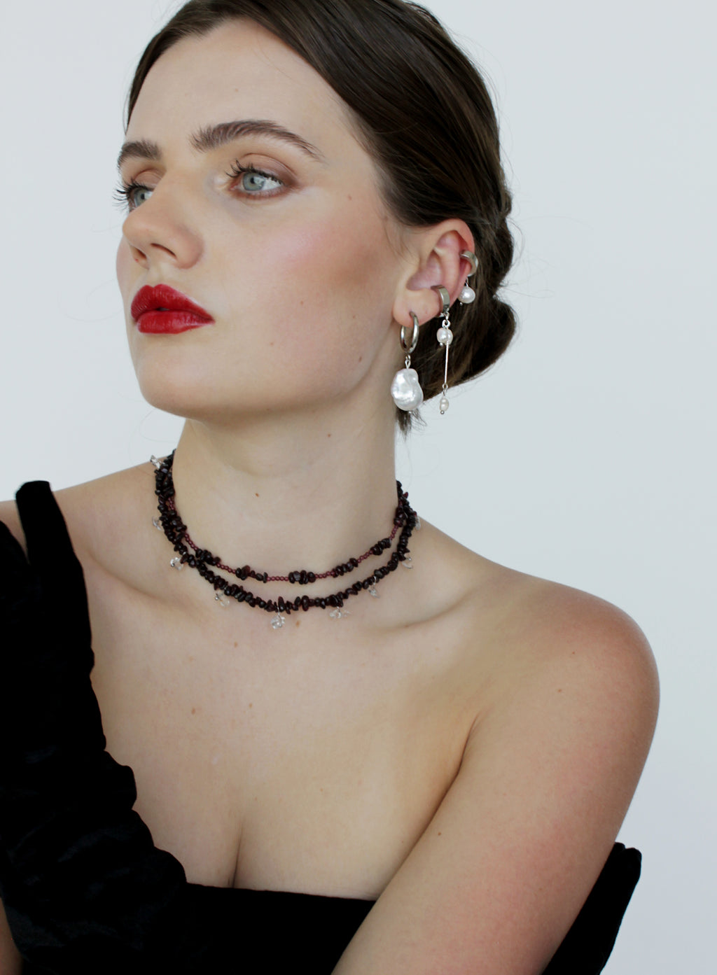 Woman wearing garnet chokers necklace and earrings with a plain background
