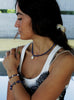 Woman with a ponytail wearing a blue beaded necklace and baraoque pearl charm and white top.