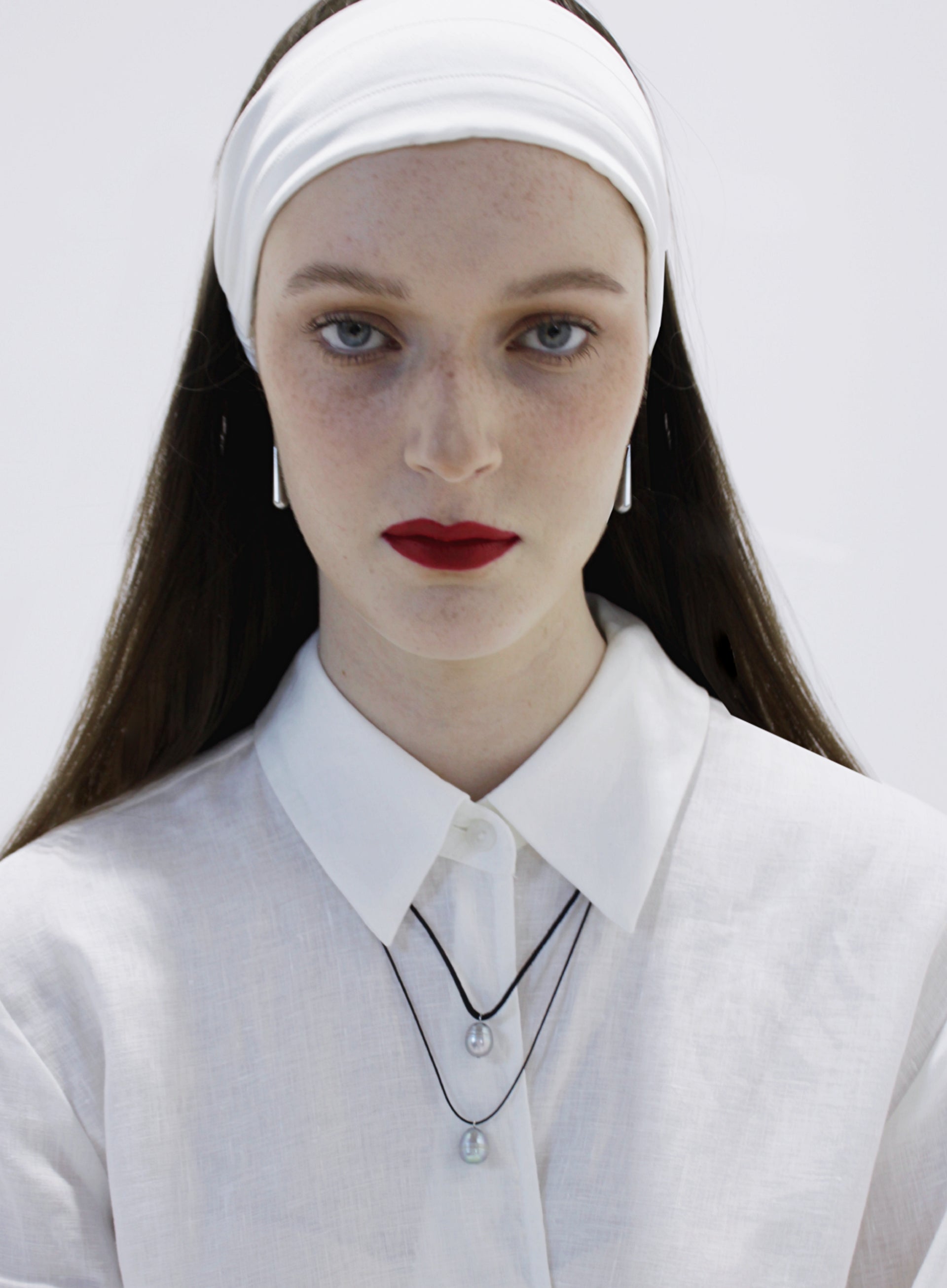 Woman wearing a white headband and a white outfit with pearl necklace