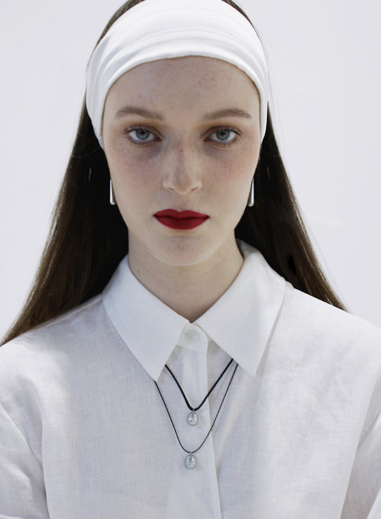Woman wearing a white headband and a white outfit with pearl necklace