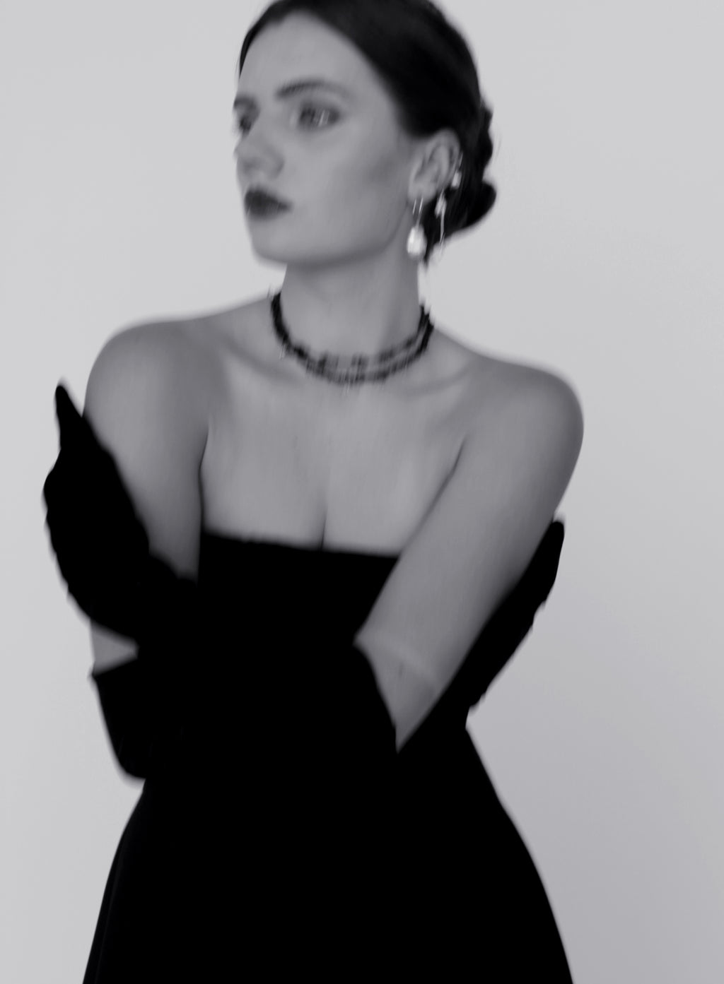 Black and white portrait of a person wearing a strapless dress and gloves against a plain background