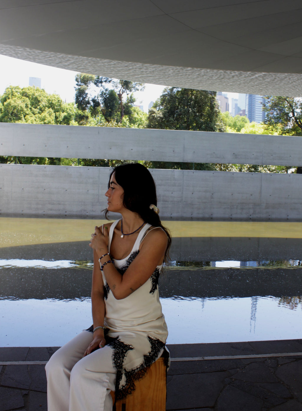 Woman with a ponytail wearing a blue beaded necklace and baraoque pearl charm and white top.