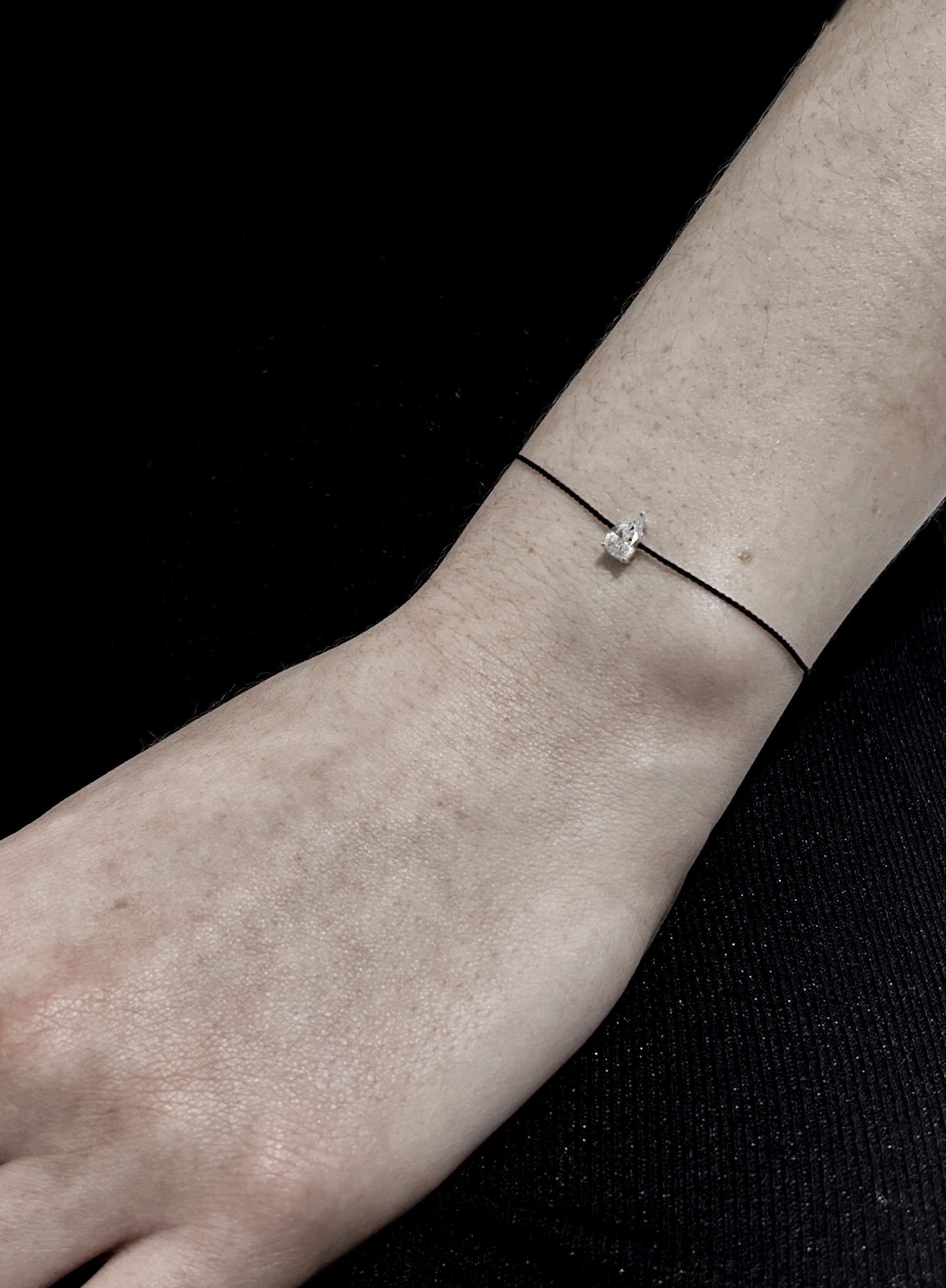 Thin bracelet with a small teardrop charm on a wrist against a black background