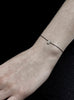 Thin bracelet with a small teardrop charm on a wrist against a black background