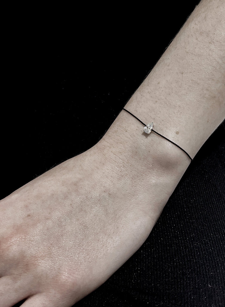 Thin bracelet with a small teardrop charm on a wrist against a black background