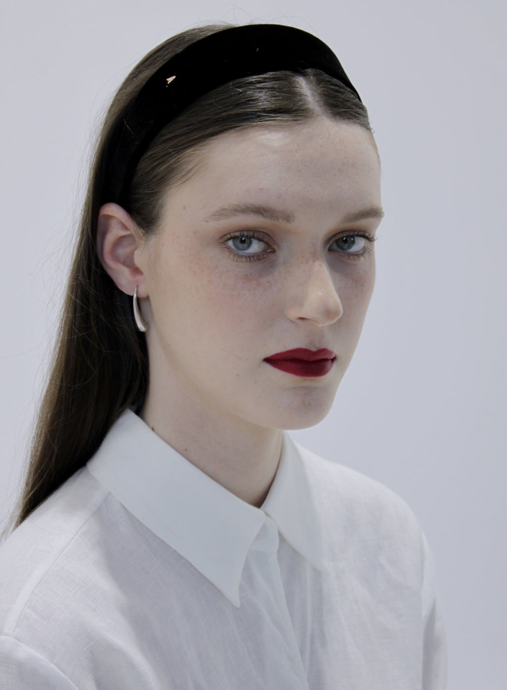 Woman wearing a black headband and white shirt against a plain background