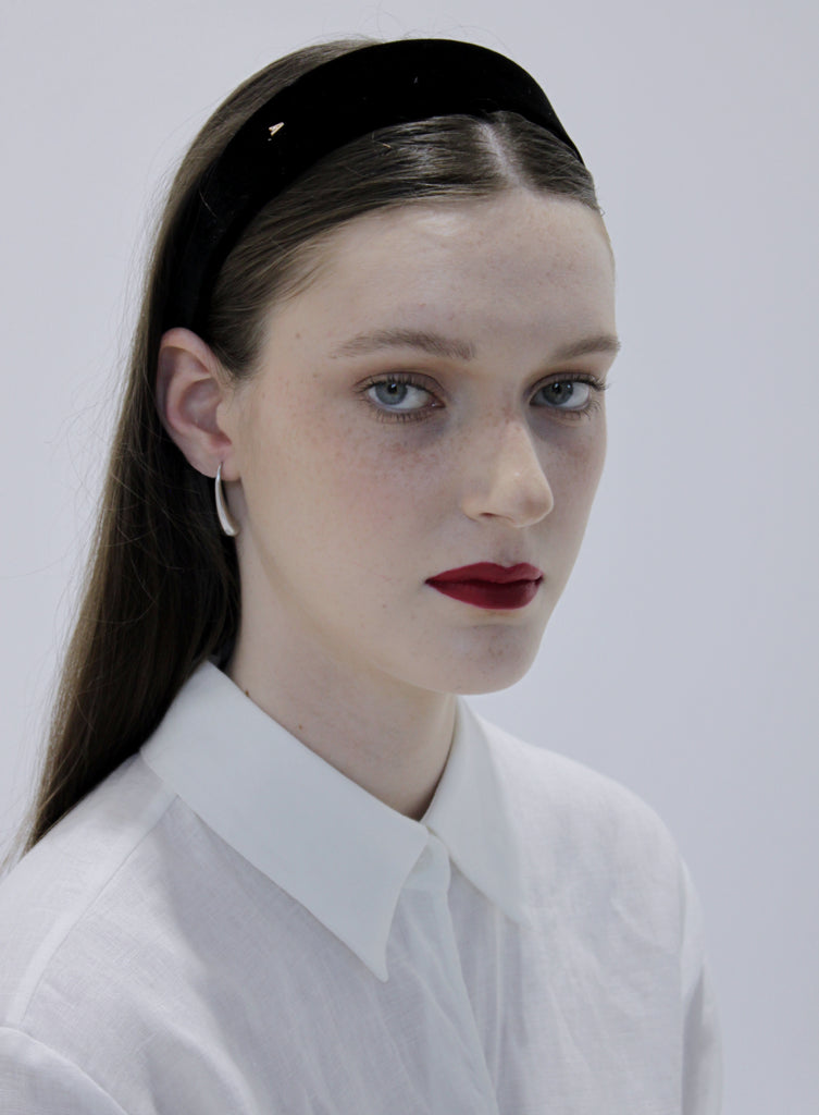 Woman wearing a black headband and white shirt against a plain background