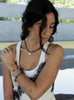 Woman with a ponytail wearing a blue beaded necklace and baraoque pearl charm and white top.