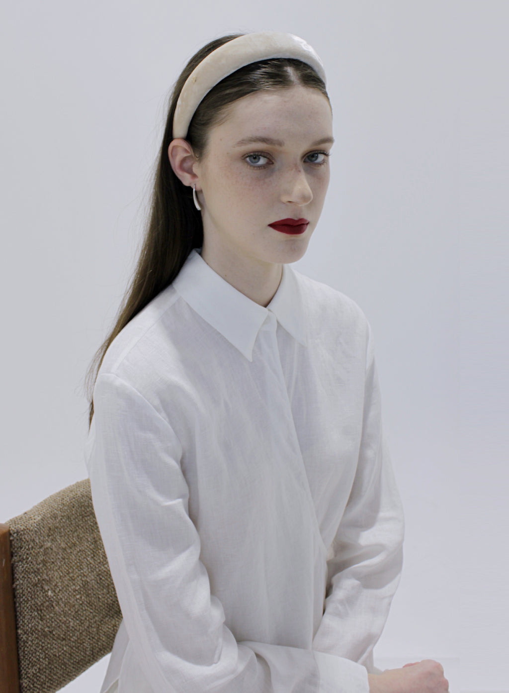 Woman wearing a white shirt and beige headband against a plain background