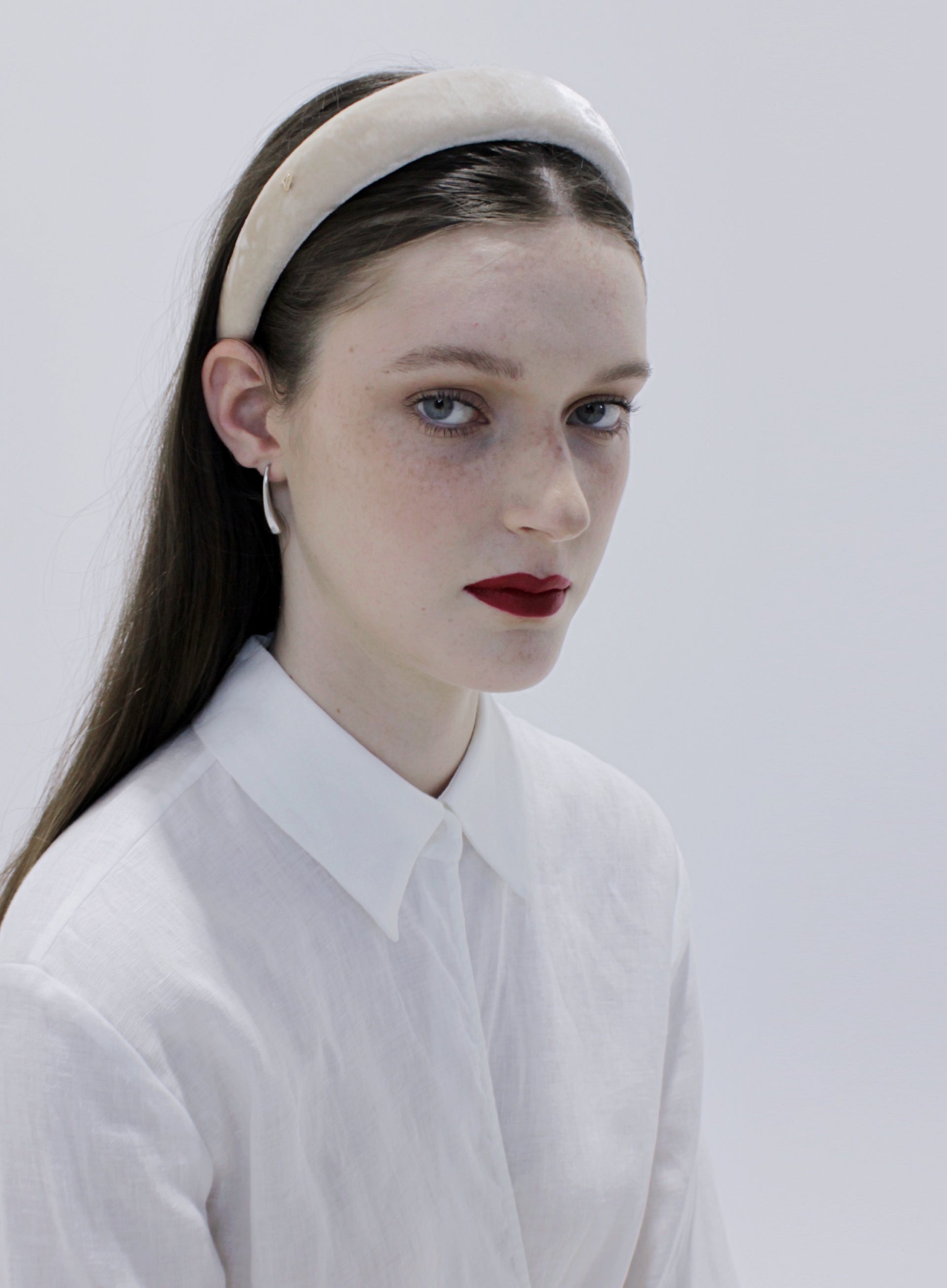 Woman wearing a white headband and white shirt against a light gray background