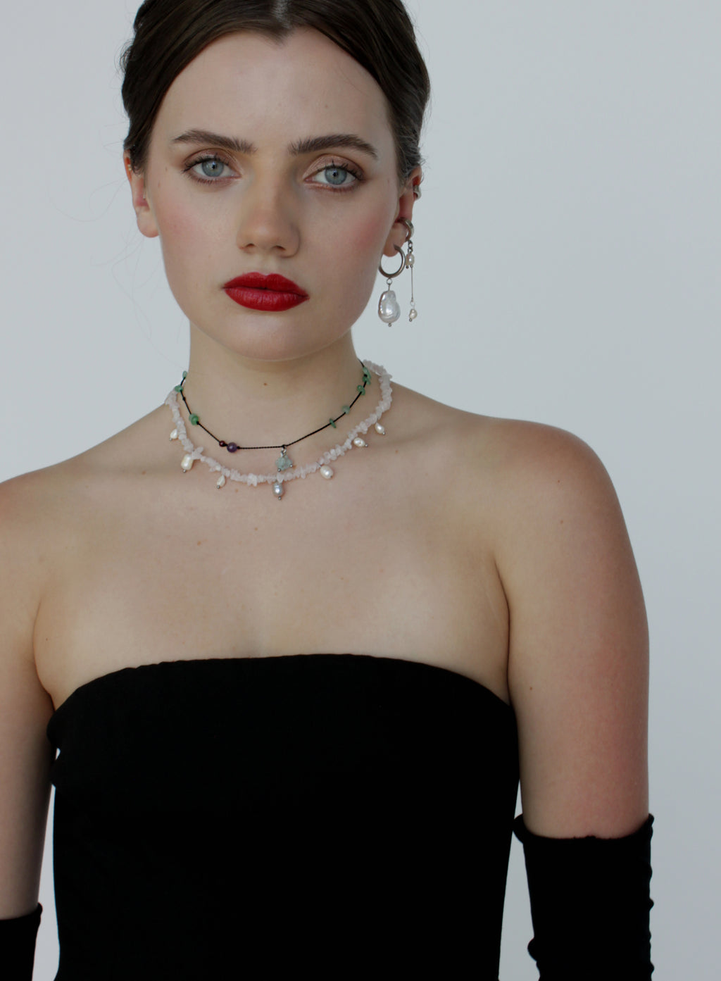 Woman wearing a black strapless dress with jewelry on a plain background