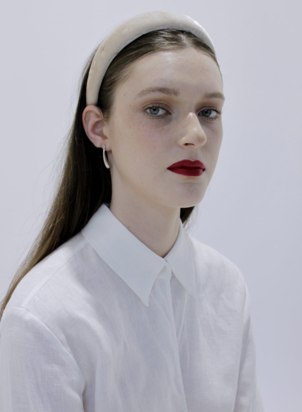 Woman wearing a white shirt and beige headband against a plain background