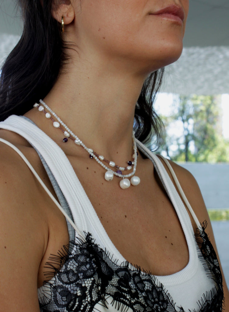 Woman wearing a white tank top with black lace details and pearl necklaces.