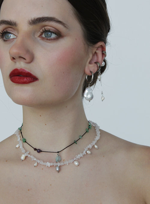 Woman wearing a pearl earring and silk cord necklace against a plain background