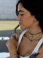 Woman wearing a white top with black lace details, multiple necklaces, and earrings.