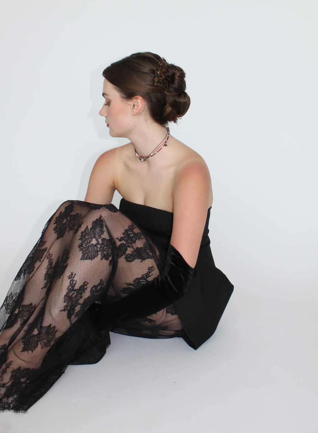Woman wearing a black lace garment sitting on a white background