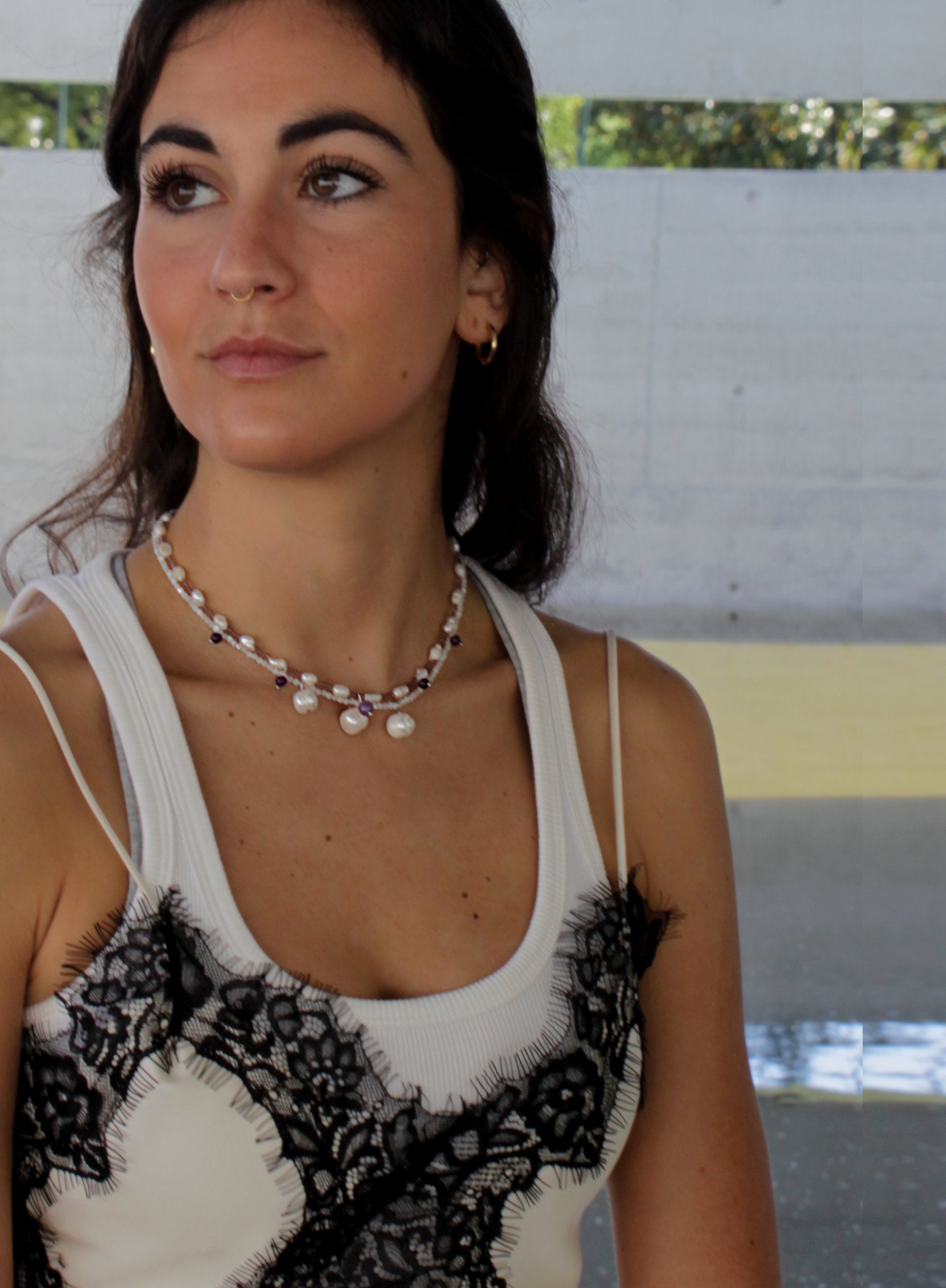 Woman wearing a white tank top with black lace details and pearl necklaces.