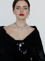 Woman wearing a black top with layered necklaces against a plain background