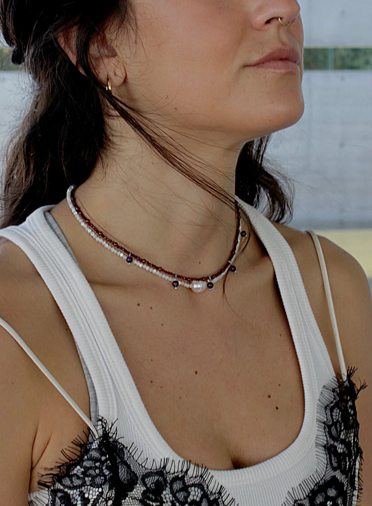 Close-up of a woman wearing a beaded pearl and garnet necklaces with a blurred background