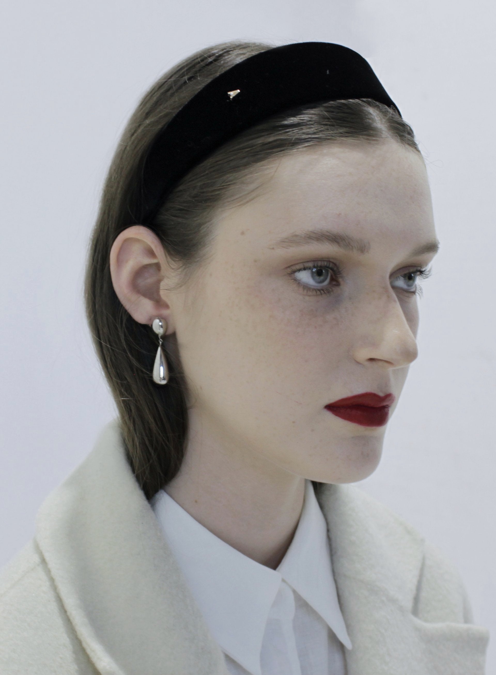 Woman wearing a black headband and pearl earrings against a white background